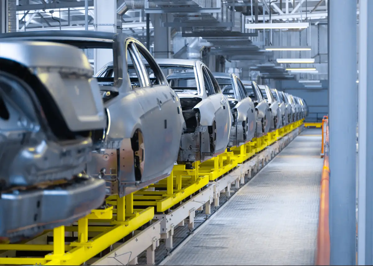 Reihe teilweise montierter Fahrzeugkarosserien steht auf einer gelben Produktionsanlage in einer modernen Fabrikhalle.