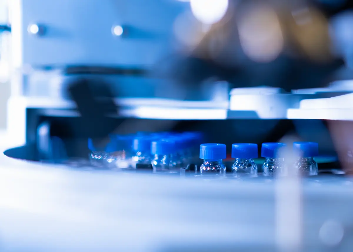 Kleine transparente Fläschchen mit blauen Verschlüssen werden in einer industriellen Produktions- oder Abfüllanlage verarbeitet.